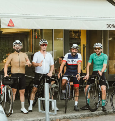 Cinq cyclistes posent avec leurs vélos devant le restaurant Dona Maria à Neuchâtel, souriants après une pause repas.