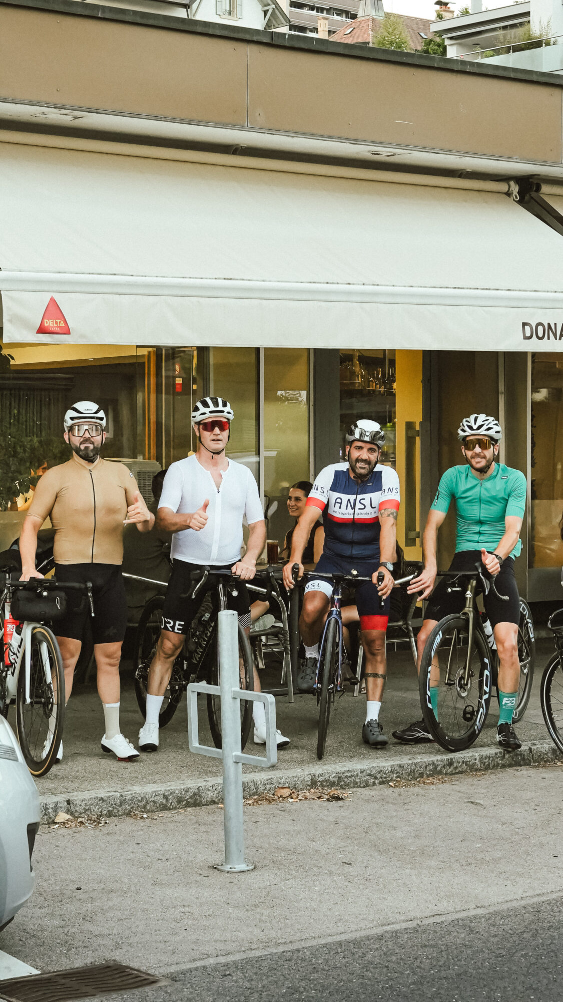Cinq cyclistes posent avec leurs vélos devant le restaurant Dona Maria à Neuchâtel, souriants après une pause repas.